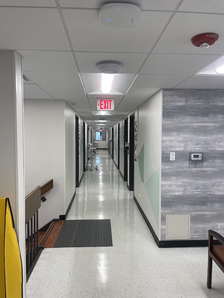 Long clinic hallway with exam rooms and exit sign