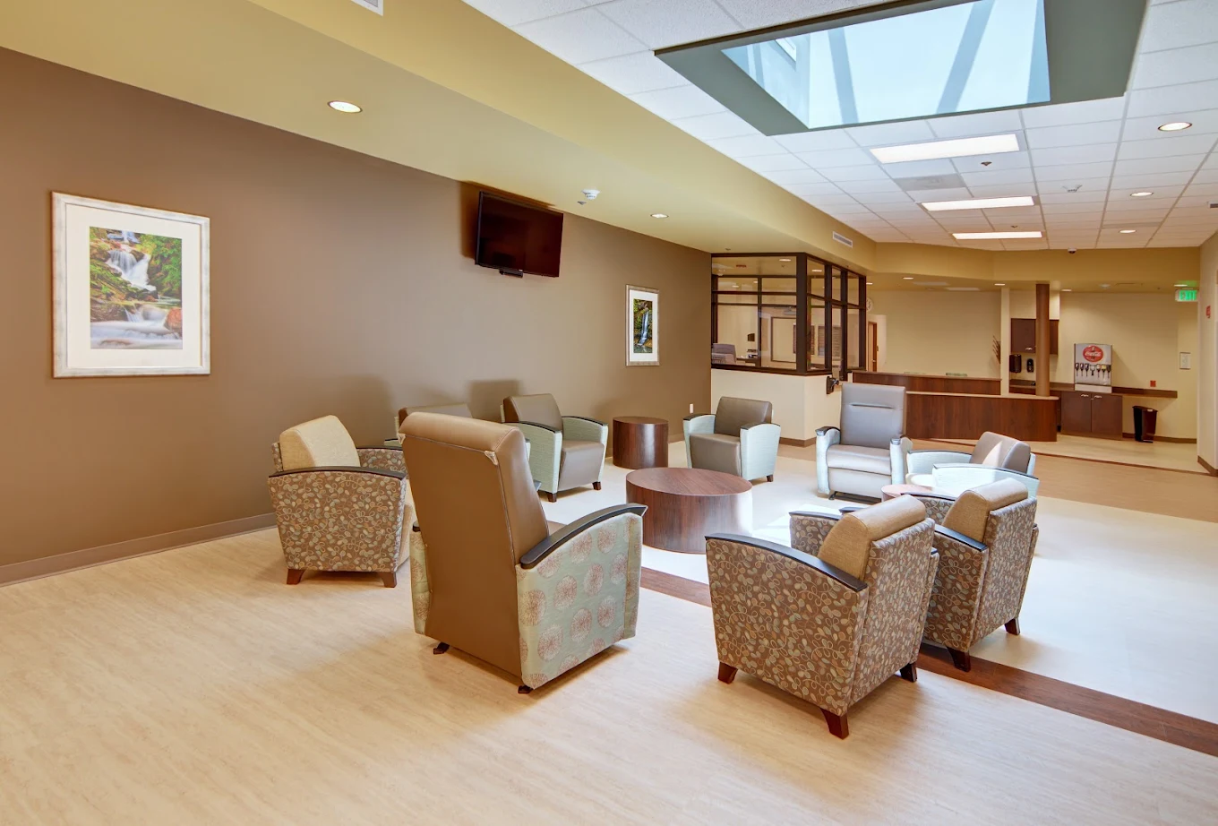 A lounge area with comfortable armchairs arranged in a circle around coffee tables, under a bright skylight near the reception area.