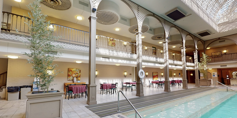 Indoor pool with elegant arched columns, a skylight casting intricate patterns, and a spacious dining area with cozy tables and warm lighting.