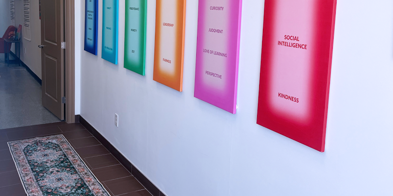  A hallway with colorful wall art showcasing positive values like wisdom, courage, and humanity. A decorative rug adds warmth to the space.