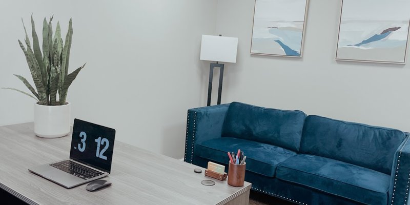 A modern, serene office space featuring a sleek desk, a vibrant blue sofa, and calming artwork, creating a comfortable and inviting environment.