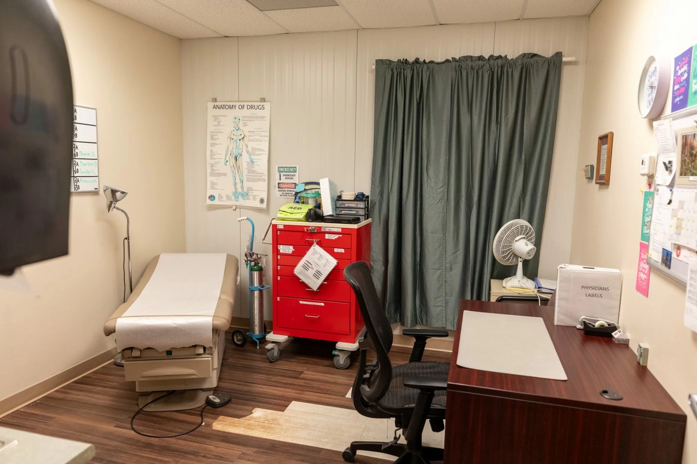 Medical examination room with exam table, desk, and emergency equipment at treatment facility