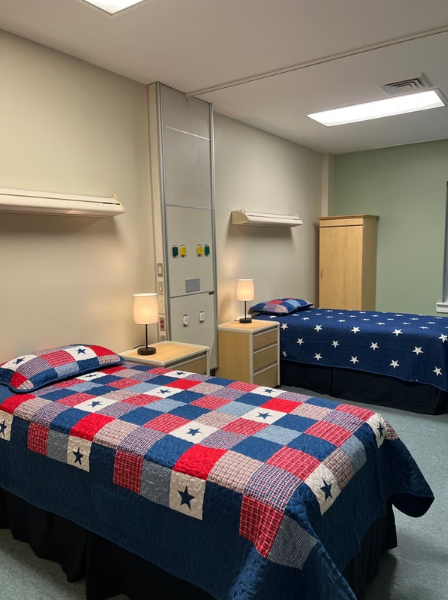 Room with two twin beds, patchwork bedding, bedside tables with lamps, and a wardrobe