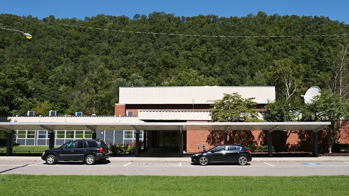 Facility exterior with parking and wooded hillside