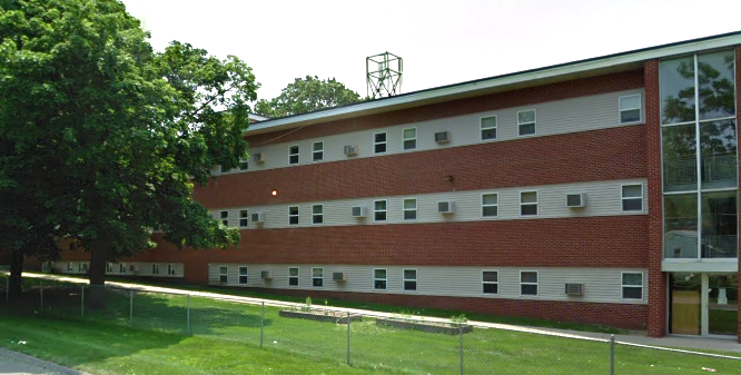 Side view of multi-story brick building with fenced lawn