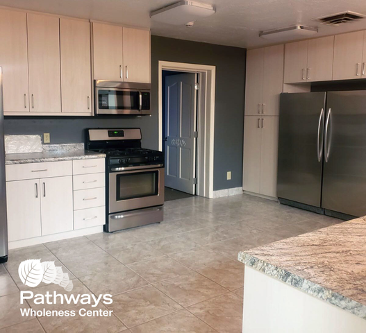 Spacious kitchen with stainless steel appliances, white cabinetry, and marble countertops at Pathways Wholeness Center
