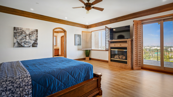 Spacious bedroom with blue bedspread, fireplace, and balcony with scenic view
