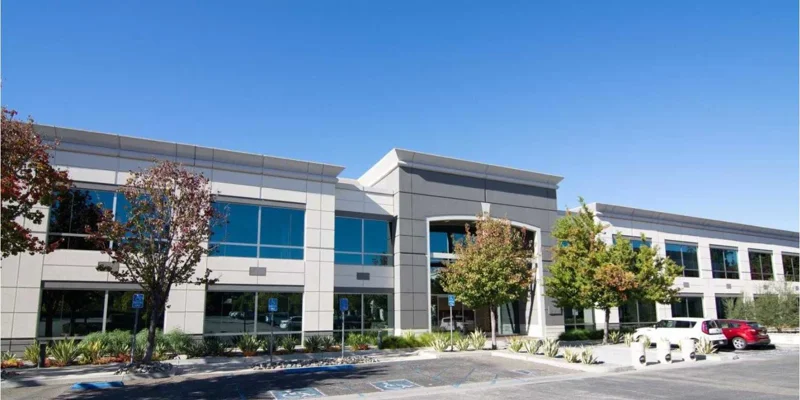 A modern, two-story rehab building with large windows and well-kept landscaping, under a bright, clear blue sky. A peaceful setting.