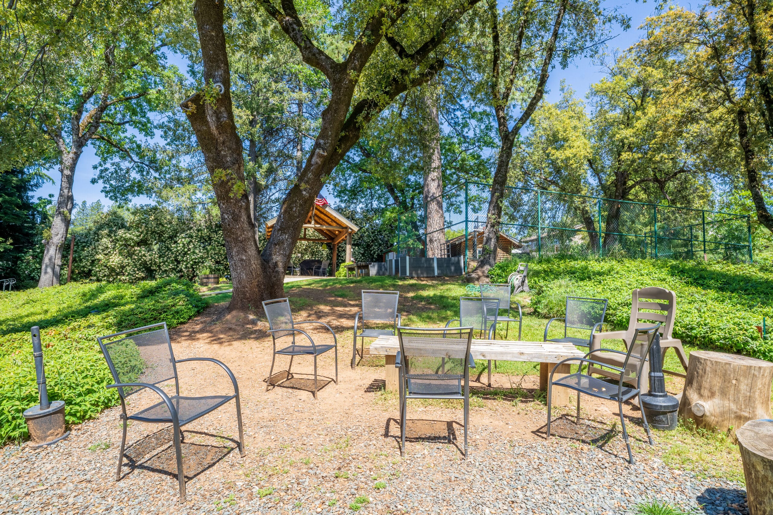 ircle of metal chairs under large oak trees, set up for group sessions or relaxation in a shaded area near a garden and pavilion