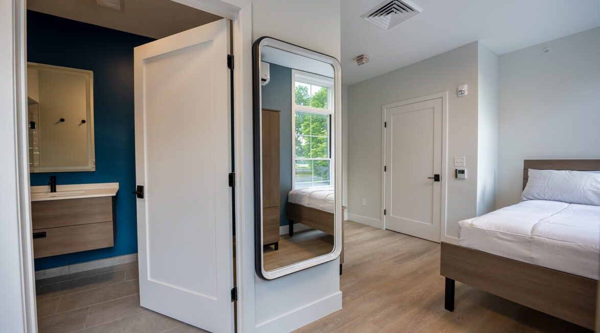 Private resident bedroom featuring an ensuite bathroom, dresser, and large mirror