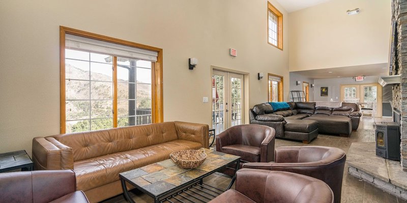 A spacious living room with large windows offering scenic views, comfortable leather seating, and a stone fireplace creating a cozy atmosphere.