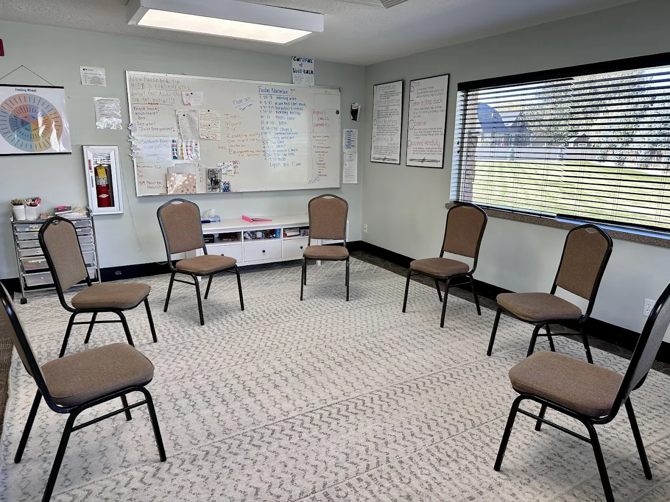 Meeting space with chairs arranged in a circle, whiteboard notes, and emotion wheel poster on the wall at New Roads Behavioral Health