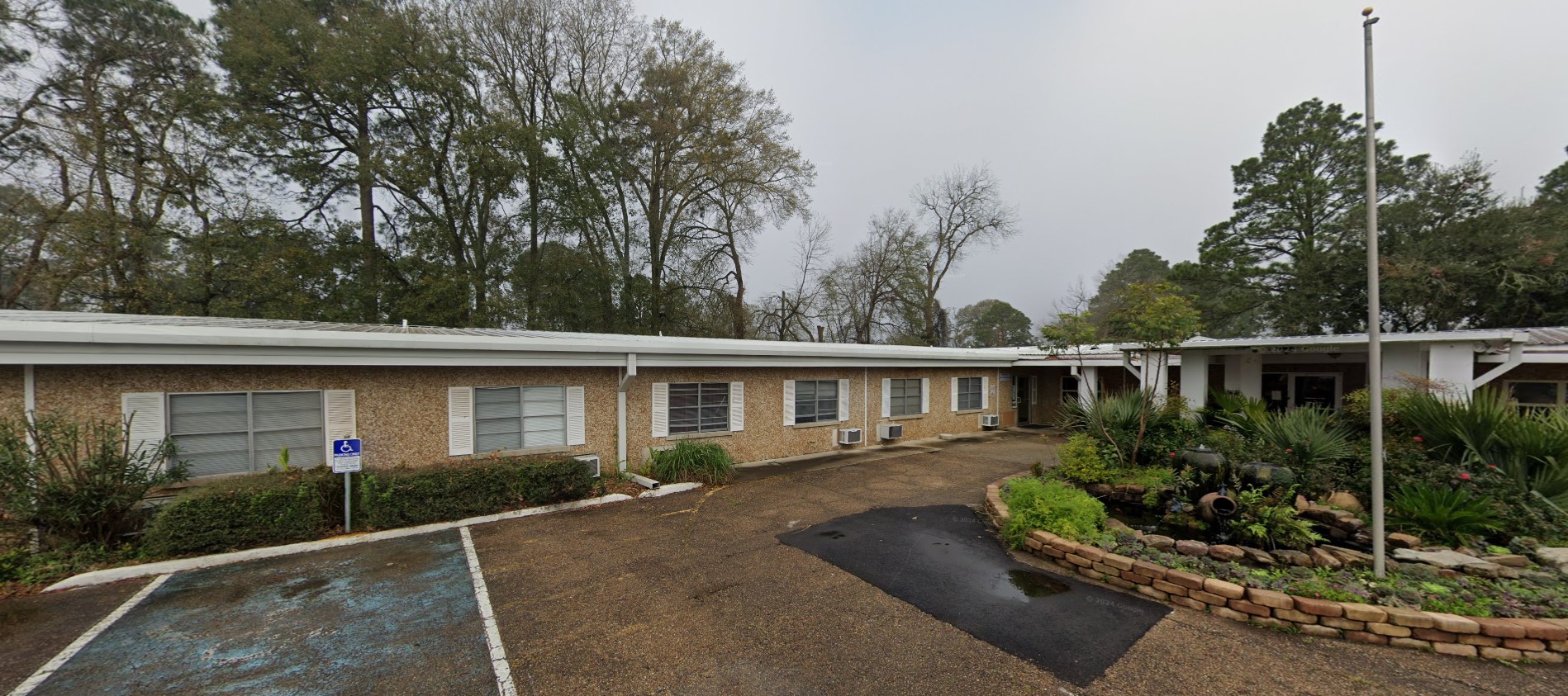A welcoming brick building with large windows and a well-maintained lawn, with trees and shrubs.