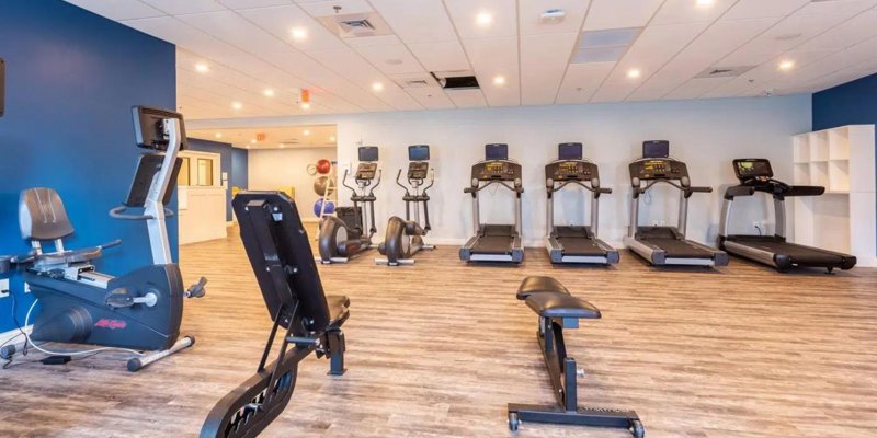 A modern fitness room with treadmills, stationary bikes, and strength equipment on wood-style flooring, offering a clean and motivating environment.