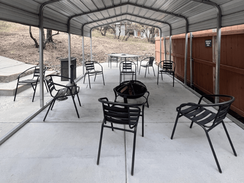 Covered patio with firepit and black chairs in wooded setting