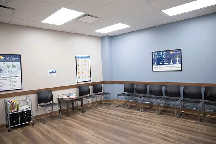 Group waiting area with rows of black chairs, educational posters, side table, and wood-look flooring