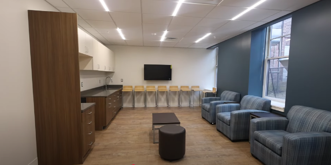 Lounge with blue chairs, kitchenette, and wall-mounted TV