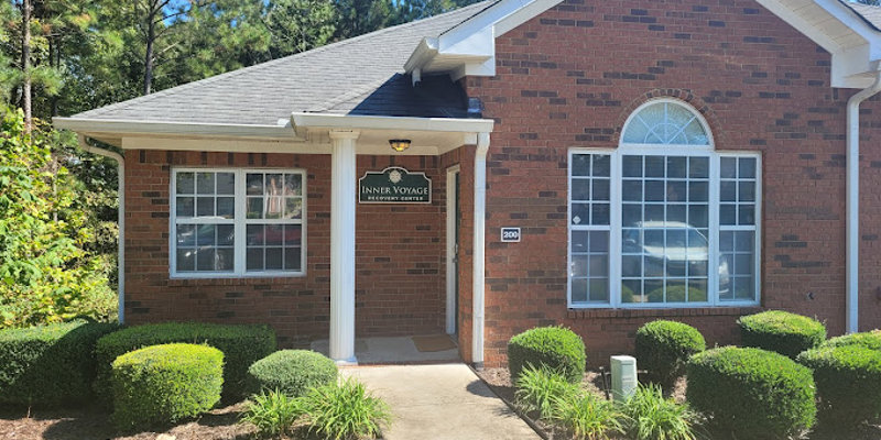  A welcoming brick building with a neatly landscaped front yard and a sign for Inner Voyage Recovery Center, surrounded by trees for privacy.