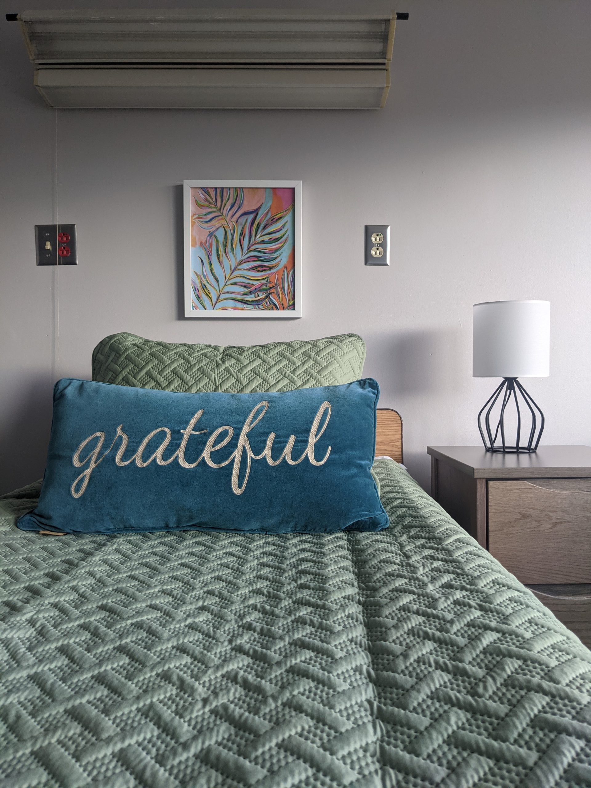 Simple bedroom with green bedding and grateful pillow