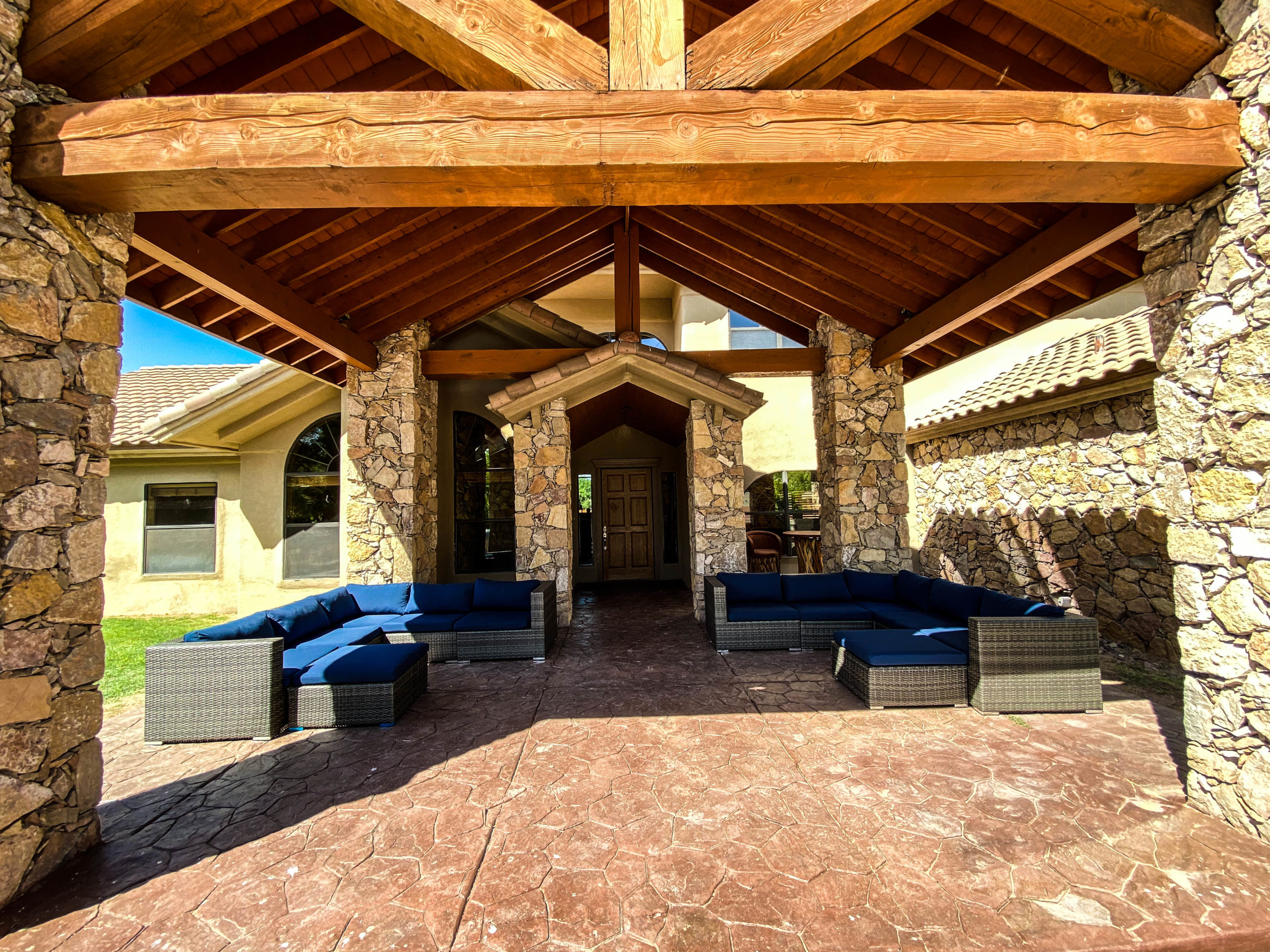 Covered patio with stone columns, exposed wooden beams, and modern cushioned seating arranged for conversation