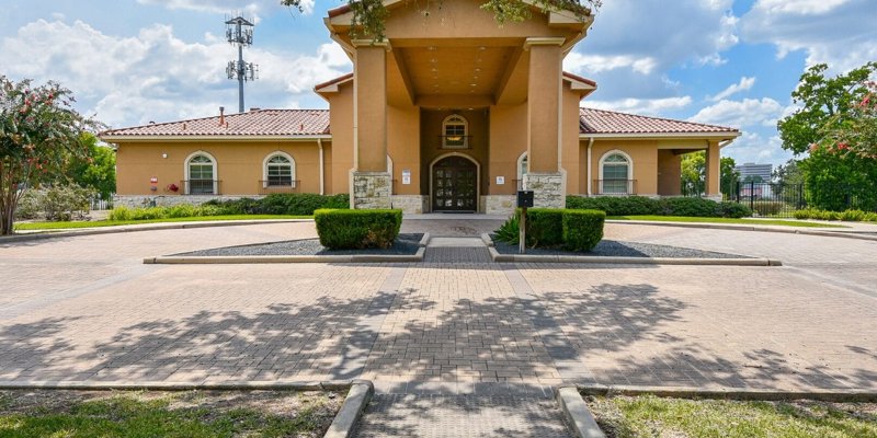  A beautiful, Mediterranean-style building with arched windows and a welcoming entrance, surrounded by well-maintained landscaping under a bright sky.