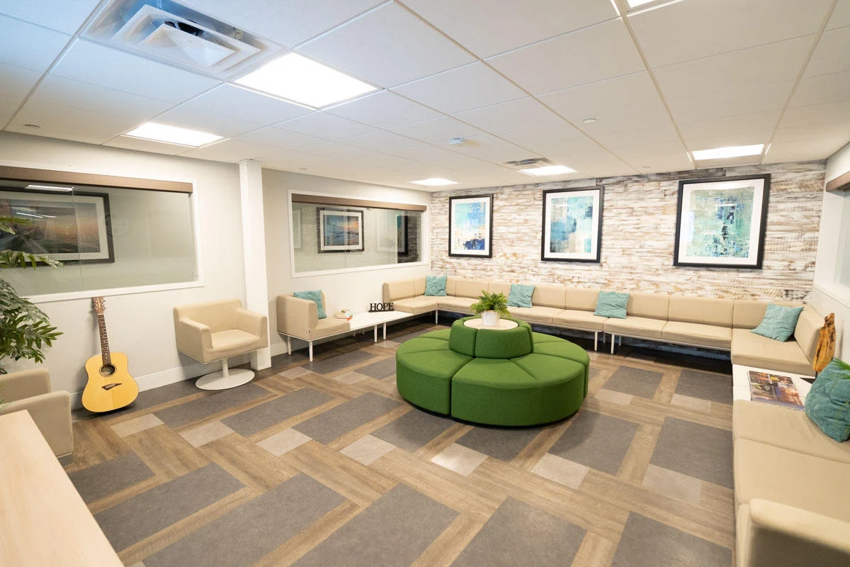 Spacious group therapy room with wrap-around seating, green circular ottoman, wall art, and warm lighting at Pine Tree Recovery Center