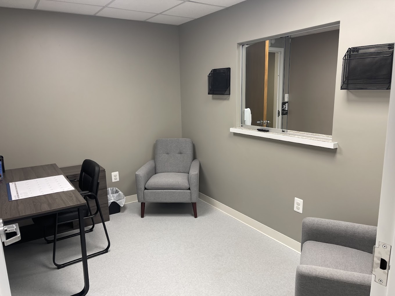 A small office with chairs, desk, and a reception window.