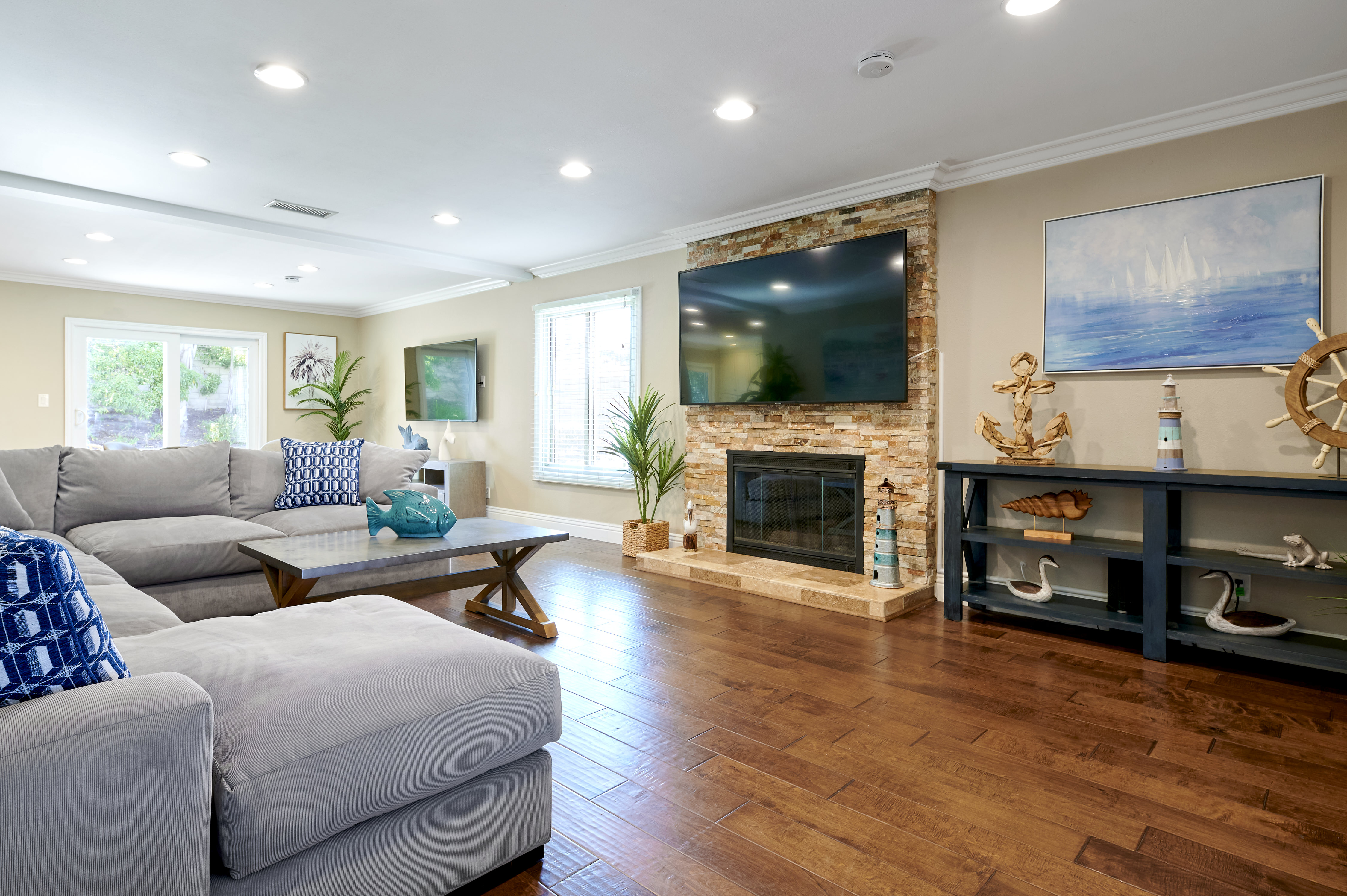  A spacious living room featuring a large sectional sofa, a stone fireplace, and coastal-themed decor, creating a bright and comfortable gathering space.