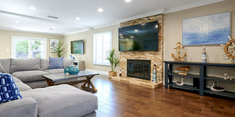  A spacious living room featuring a large sectional sofa, a stone fireplace, and coastal-themed decor, creating a bright and comfortable gathering space.