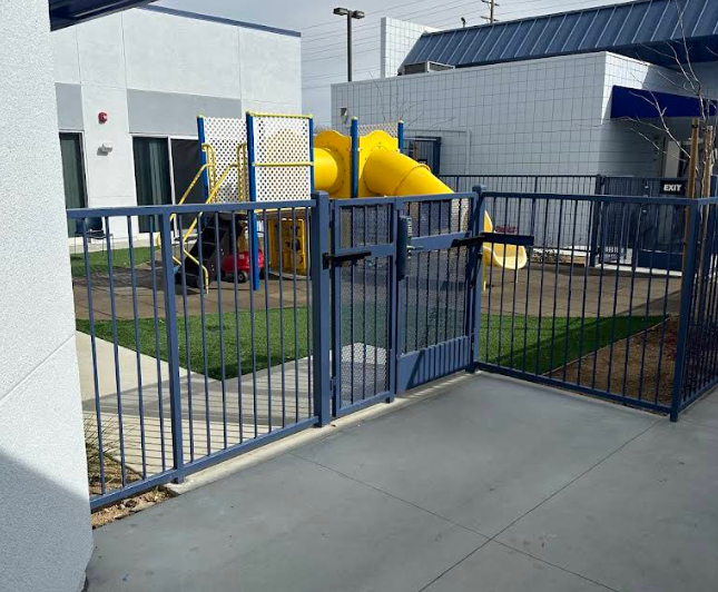 Gated playground with a yellow slide and turf
