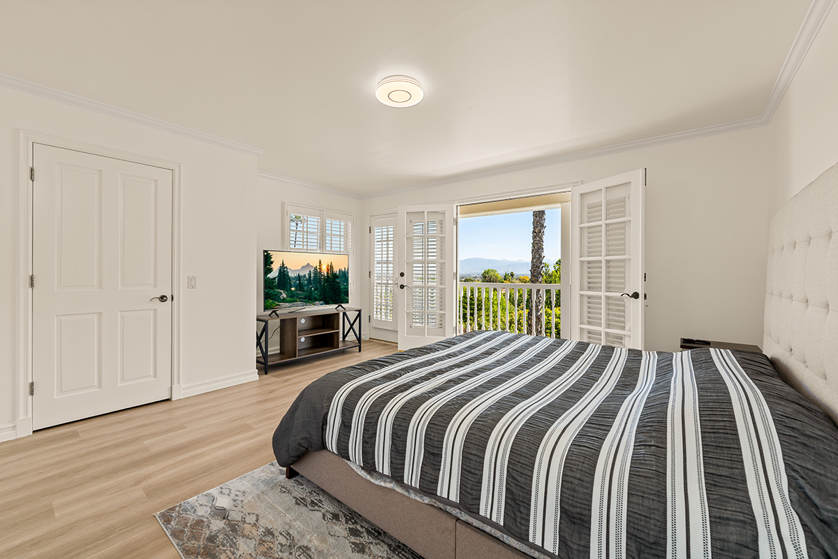 A bright bedroom with a balcony and scenic hillside views.