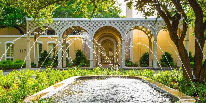 Serene courtyard featuring a fountain framed by elegant arches and lush greenery, offering a tranquil and inviting ambiance.