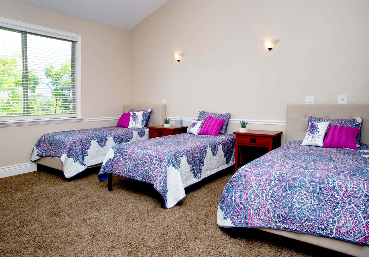Shared bedroom with three neatly made beds and natural light.