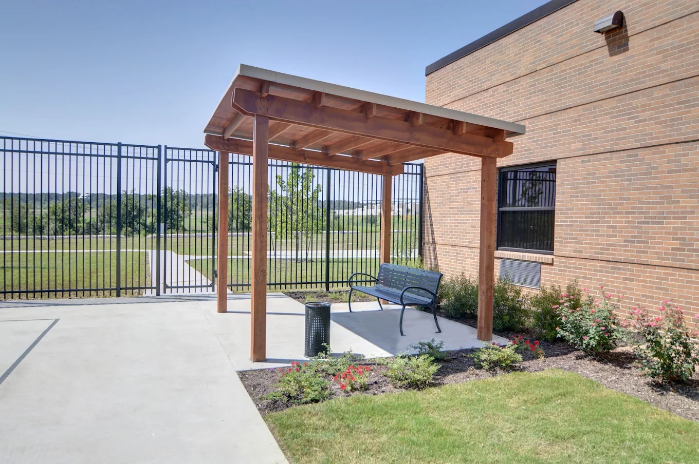 A wooden pergola over a bench surrounded by landscaped plants and flowers, offering a quiet outdoor space for rest