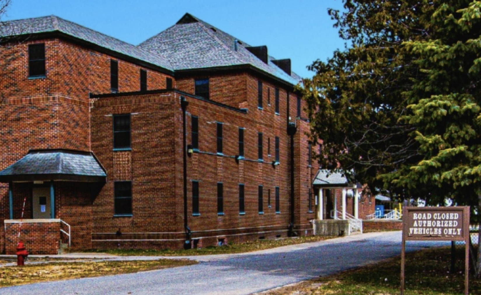 Multi-story red brick facility building along a tree-lined street