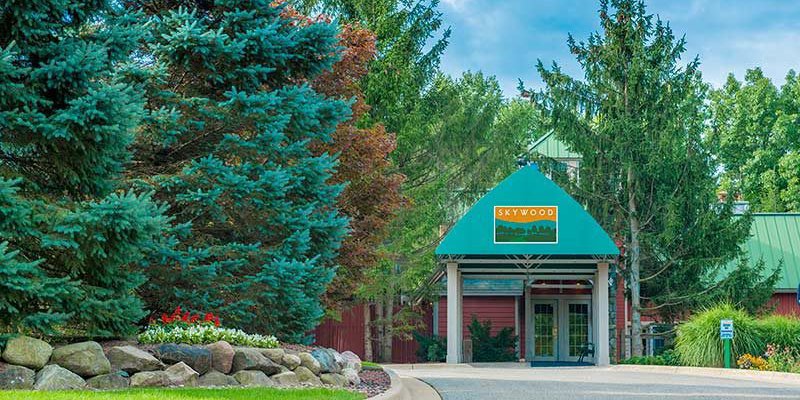 A welcoming entrance with a green roof stands surrounded by lush trees and manicured landscaping.