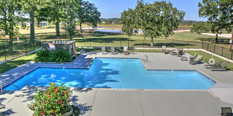 A spacious outdoor pool area surrounded by lush greenery, offering a relaxing setting with lounge chairs, vibrant flowers, and clear skies.