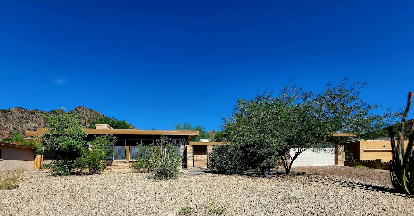Exterior of a single-story building with desert landscaping, trees, and a mountain backdrop under a clear blue sky