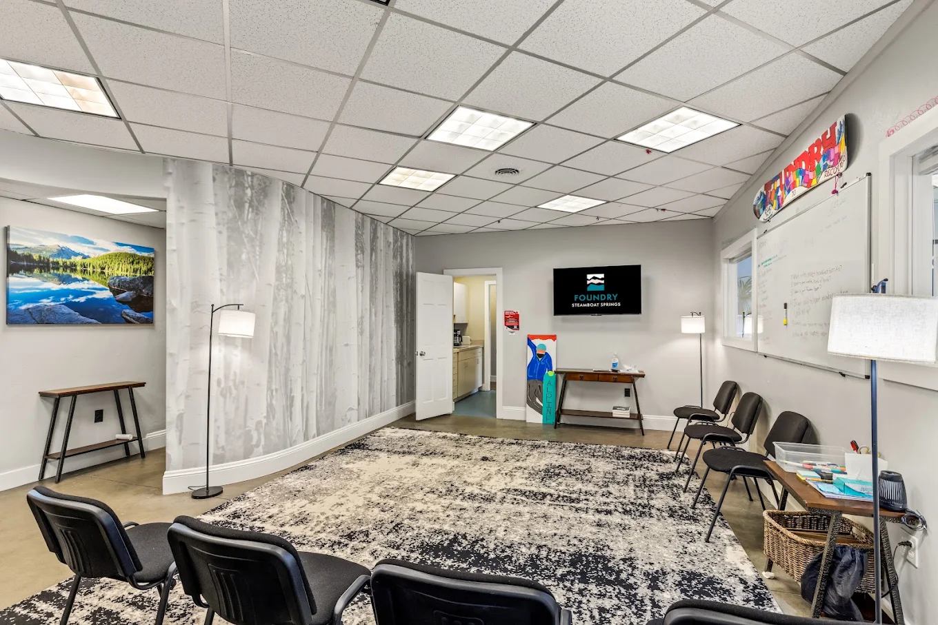 Group therapy room with chairs, large area rug, whiteboard, nature artwork, and Foundry display screen