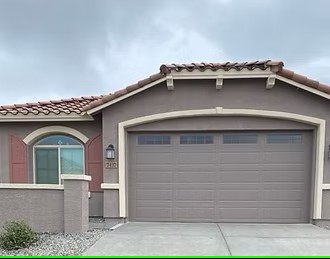 Brown garage and stucco exterior with arched entry and tile roof