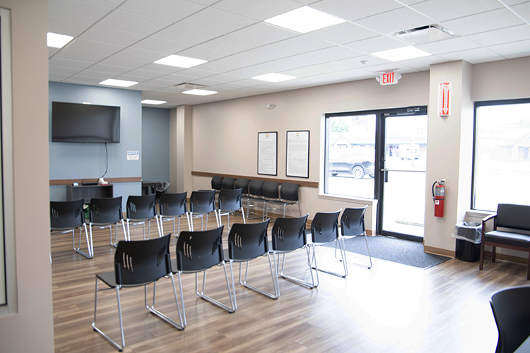 BrightView Health lobby with rows of black chairs, television, wood-look flooring, and glass entrance doors