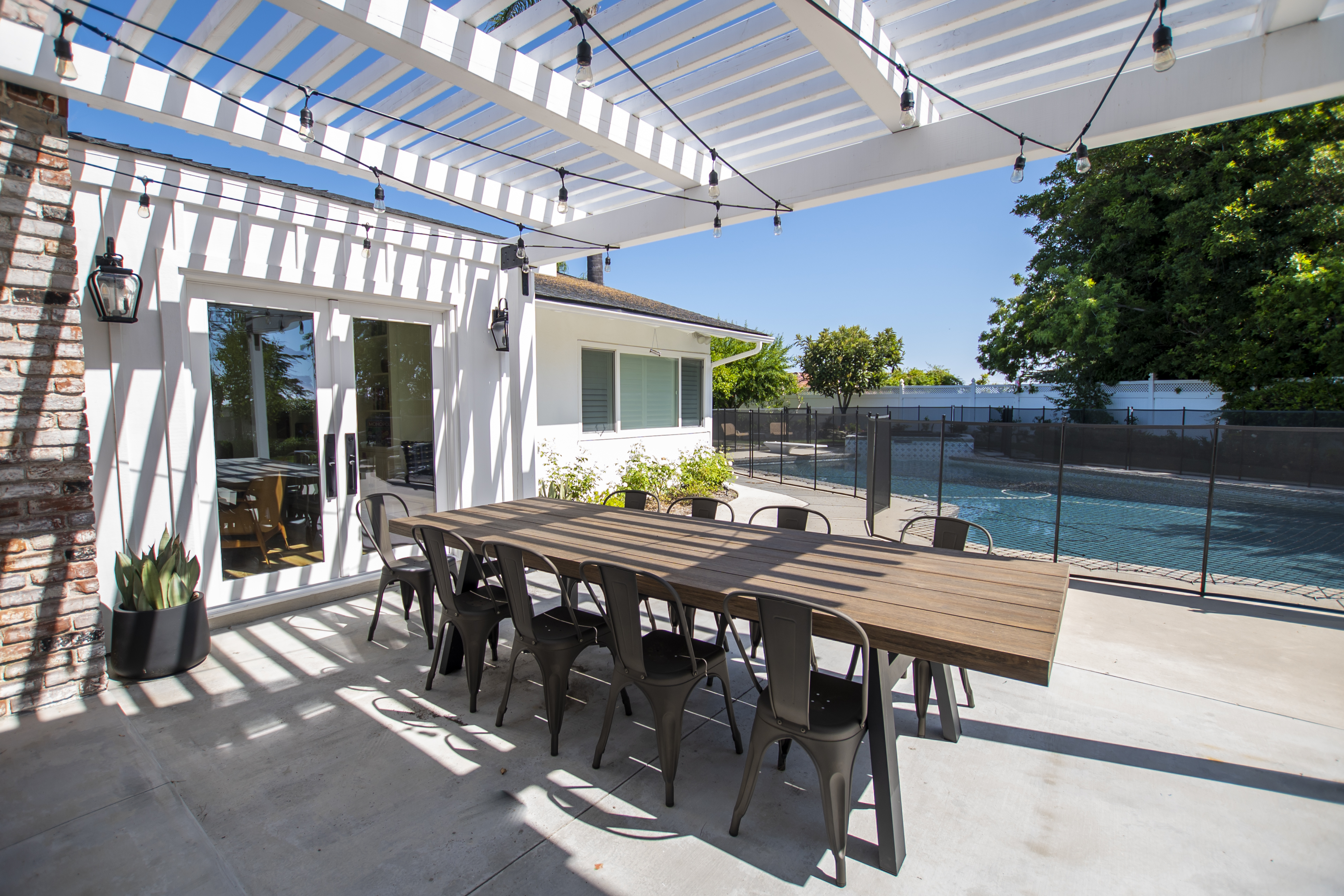 Long table under pergola beside fenced pool