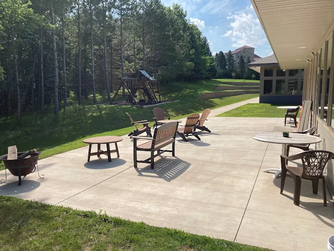 Patio with chairs, tables, and fire pit surrounded by greenery
