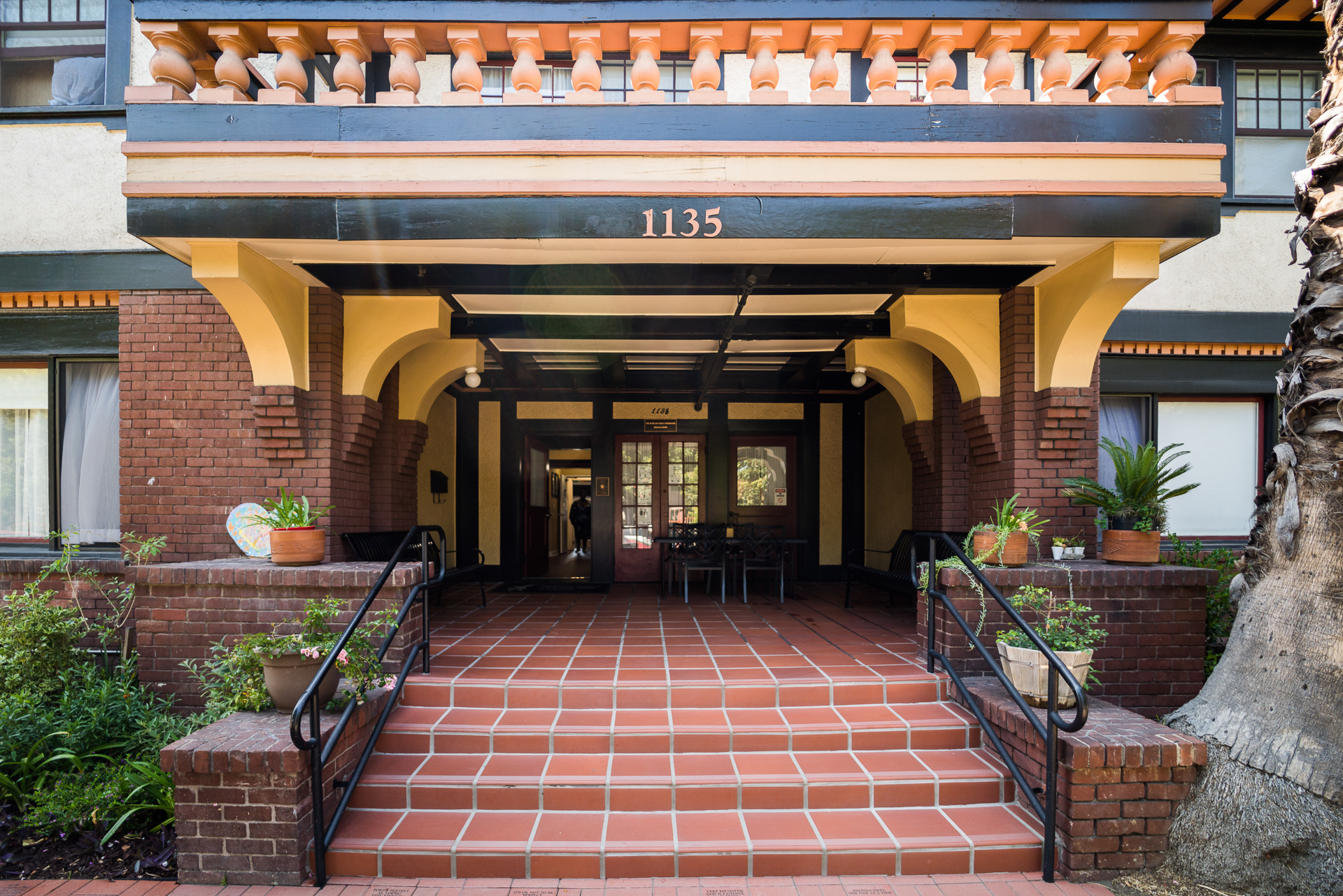 Wide tiled stairway leading to covered main entrance with potted plants
