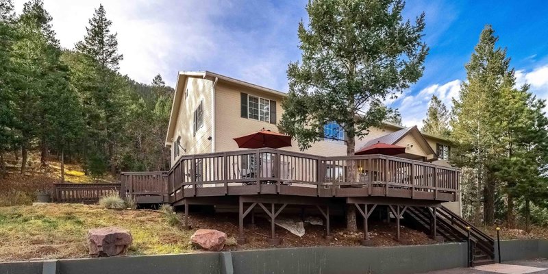 A cozy, two-story home with a spacious wooden deck surrounded by tall trees and mountain views, offering a serene, natural retreat.