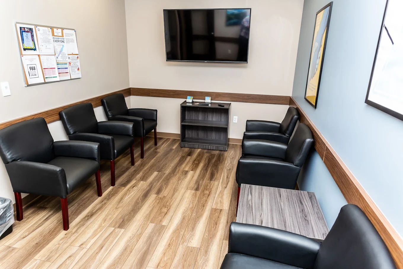 Waiting area with black chairs, tables, and wall-mounted TV