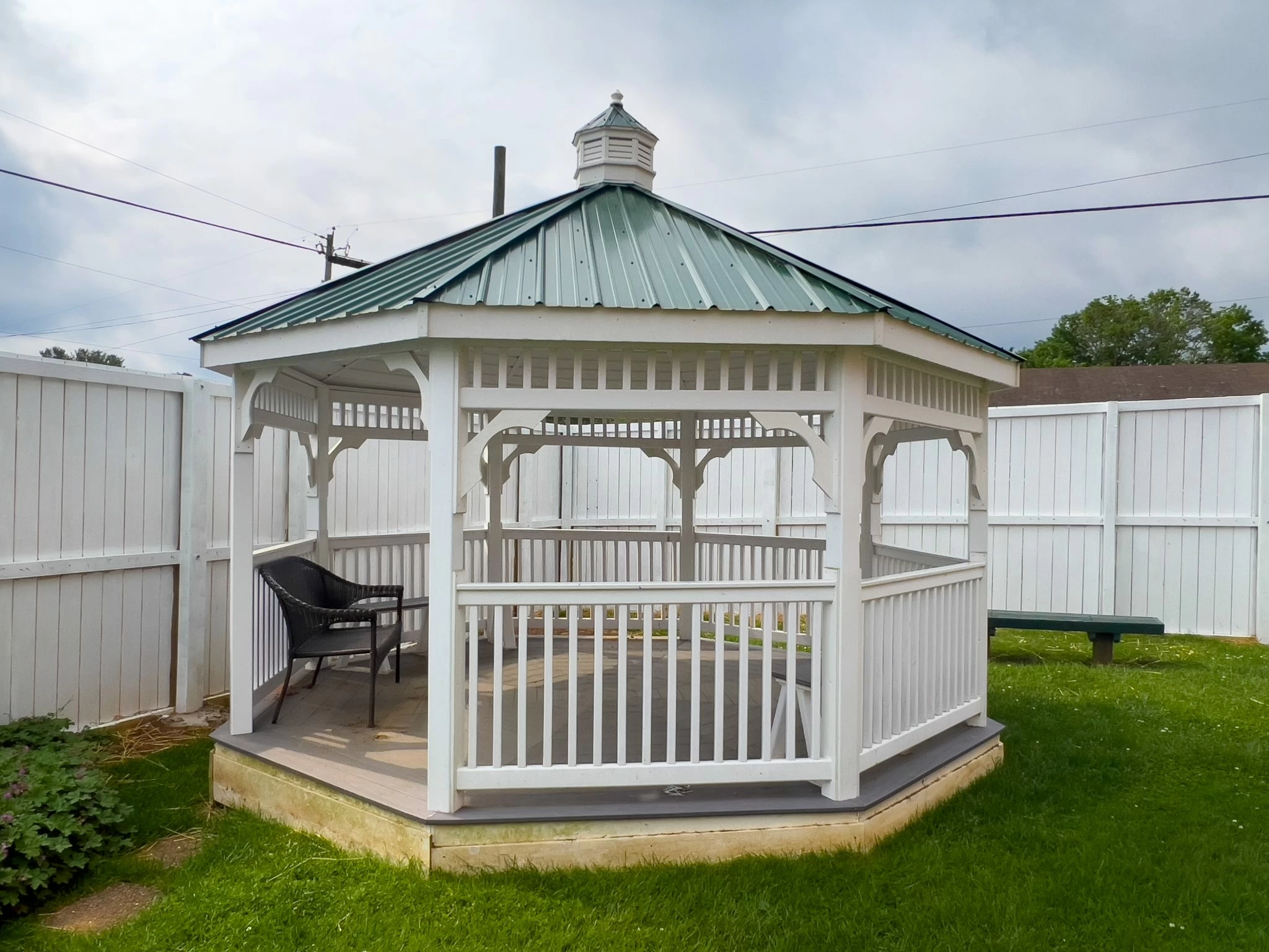 White gazebo with seating in a fenced garden area