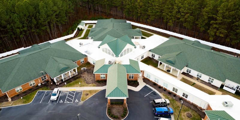 Aerial view of a spacious, modern facility with green roofs, surrounded by a serene forest, ample parking, and well-maintained pathways.