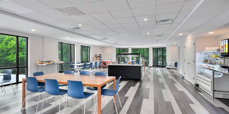 Bright and modern dining area with large windows offering serene views of greenery, complemented by sleek furniture and ample natural light.