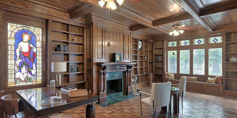 A warm and elegant study with rich wood paneling, a cozy fireplace, built-in bookshelves, stained glass accents, and comfortable seating.